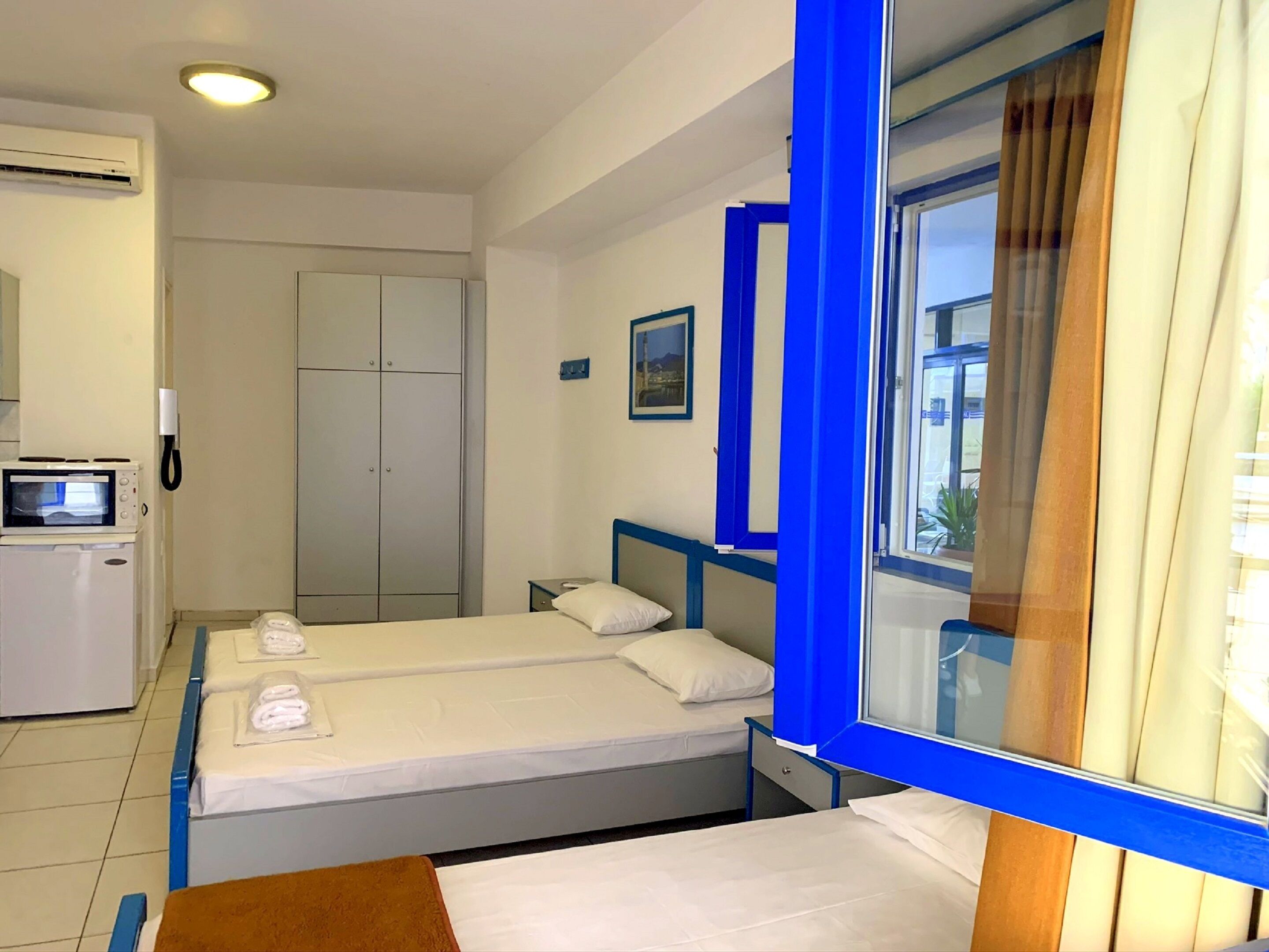 Quarto de hotel com duas camas, uma escrivaninha, um guarda-roupa, um ar condicionado e uma janela com cortinas.