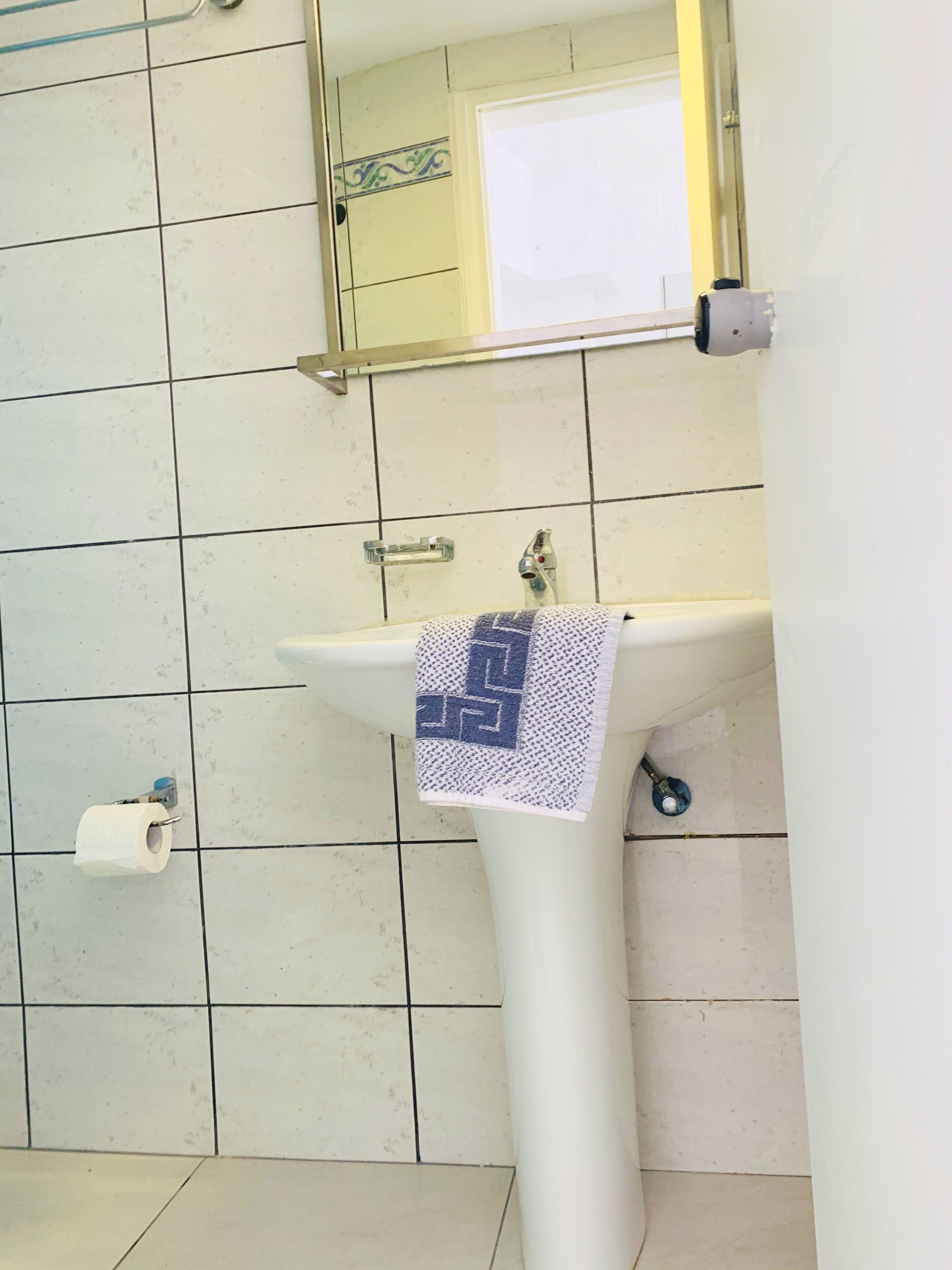 A bathroom with a white sink, a towel hanging on the faucet, a toilet paper roll, and a mirror above the sink.