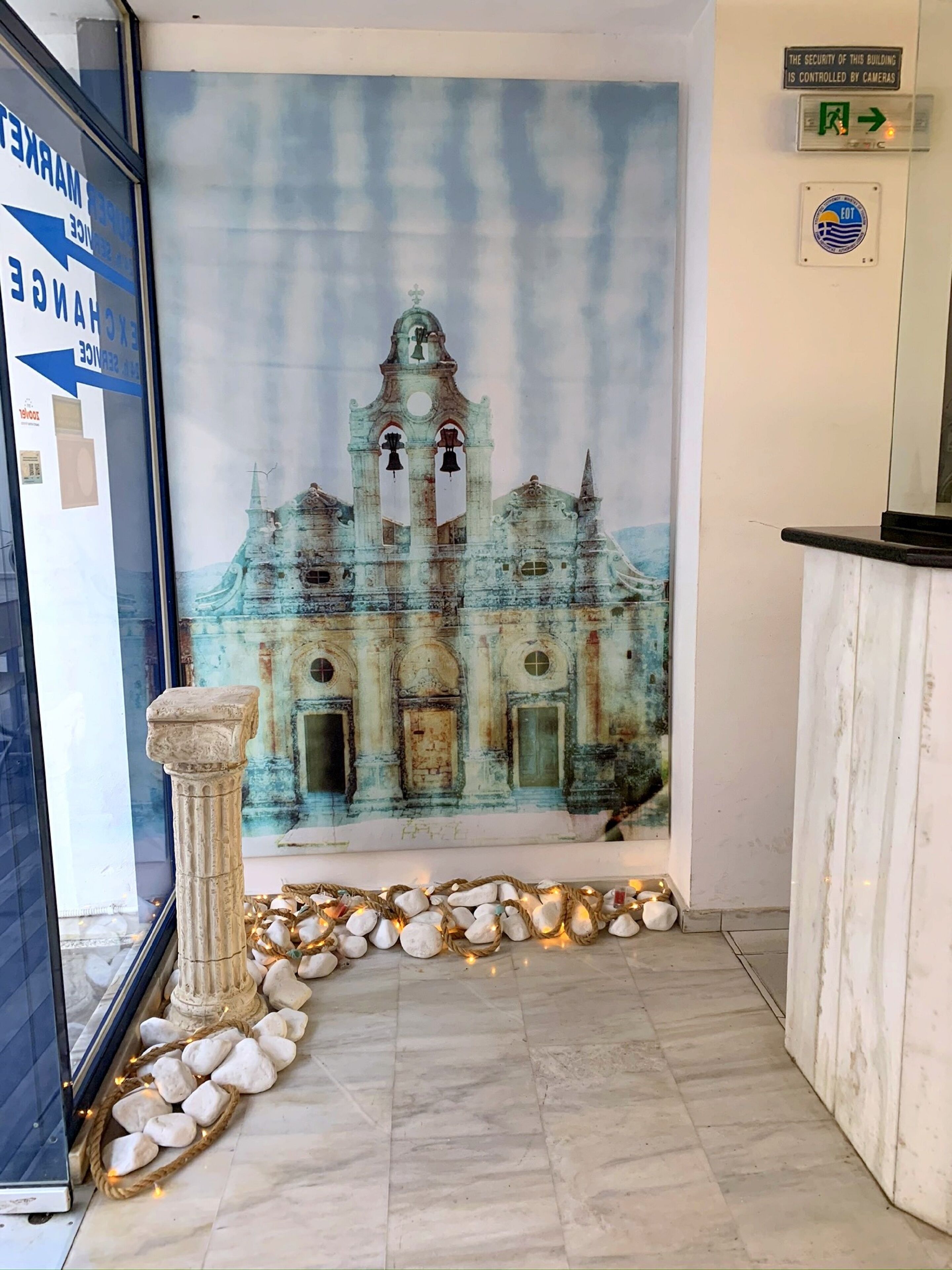 Un espace d’accueil agrémenté d’une fresque représentant un bâtiment historique, d’un sol en marbre et d’un pilier en pierre.