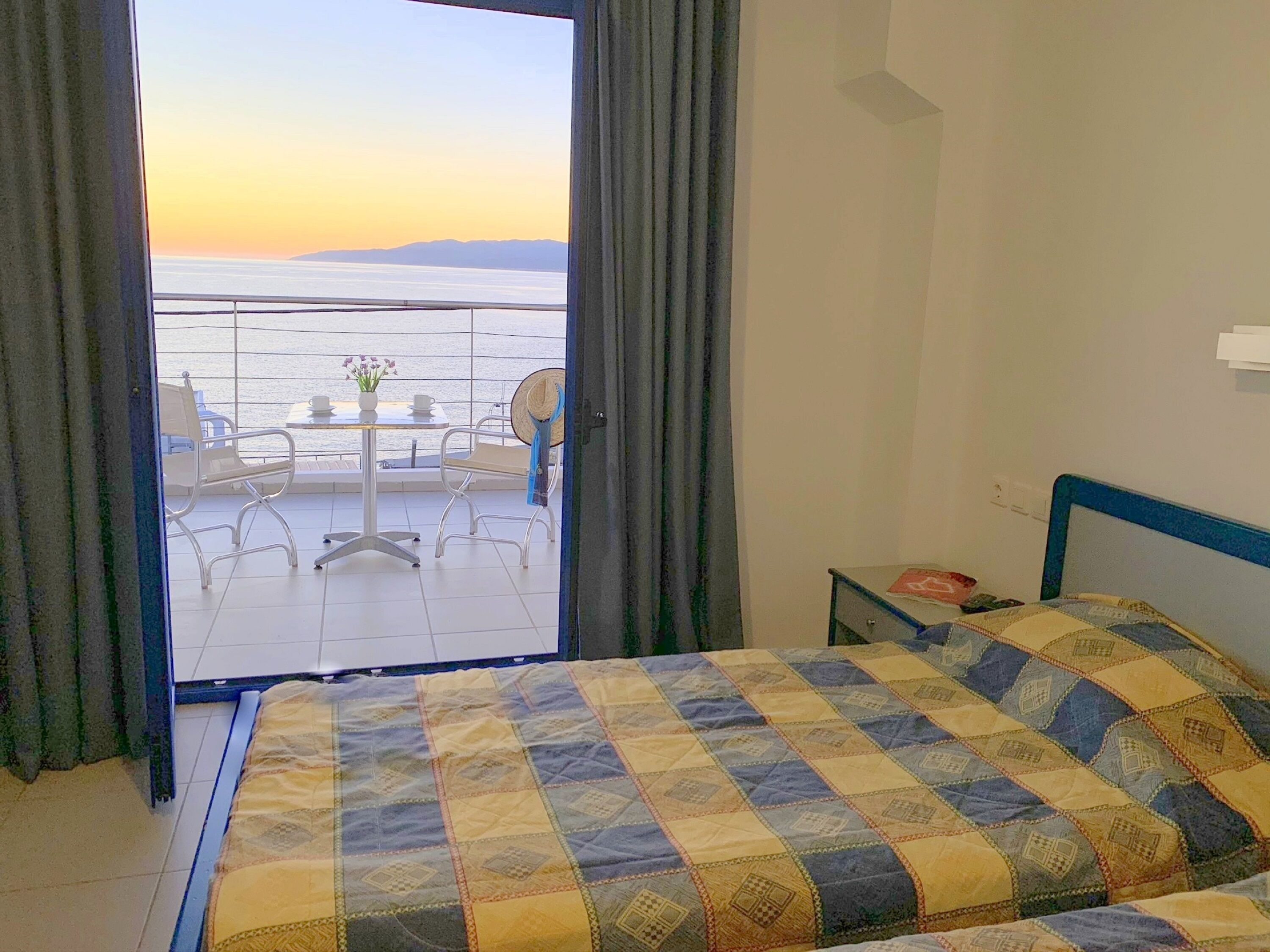 A hotel room with a bed, a small table with chairs, and a view of the sea.