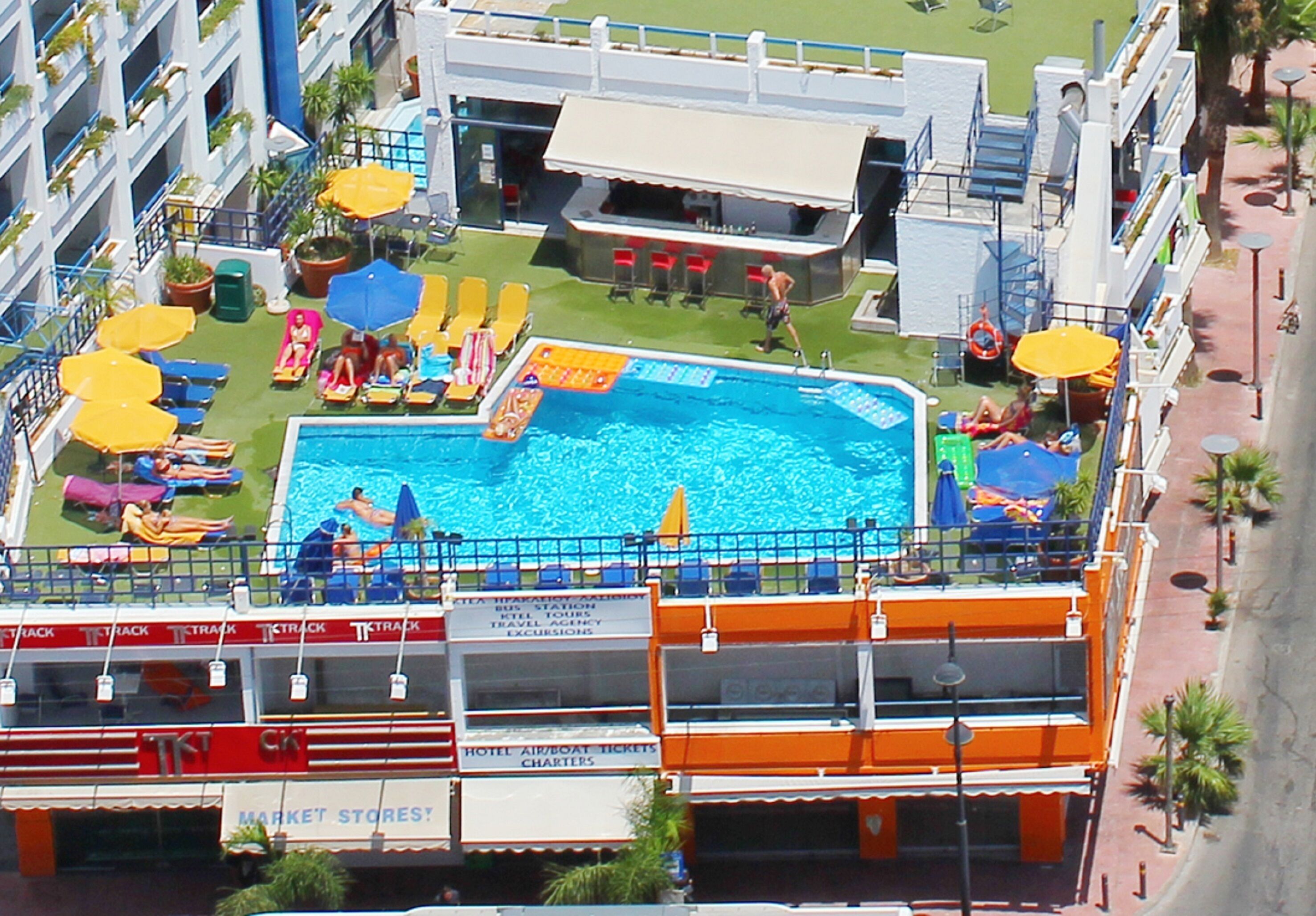 Ett hotell med en swimmingpool, solstolar och en bar.