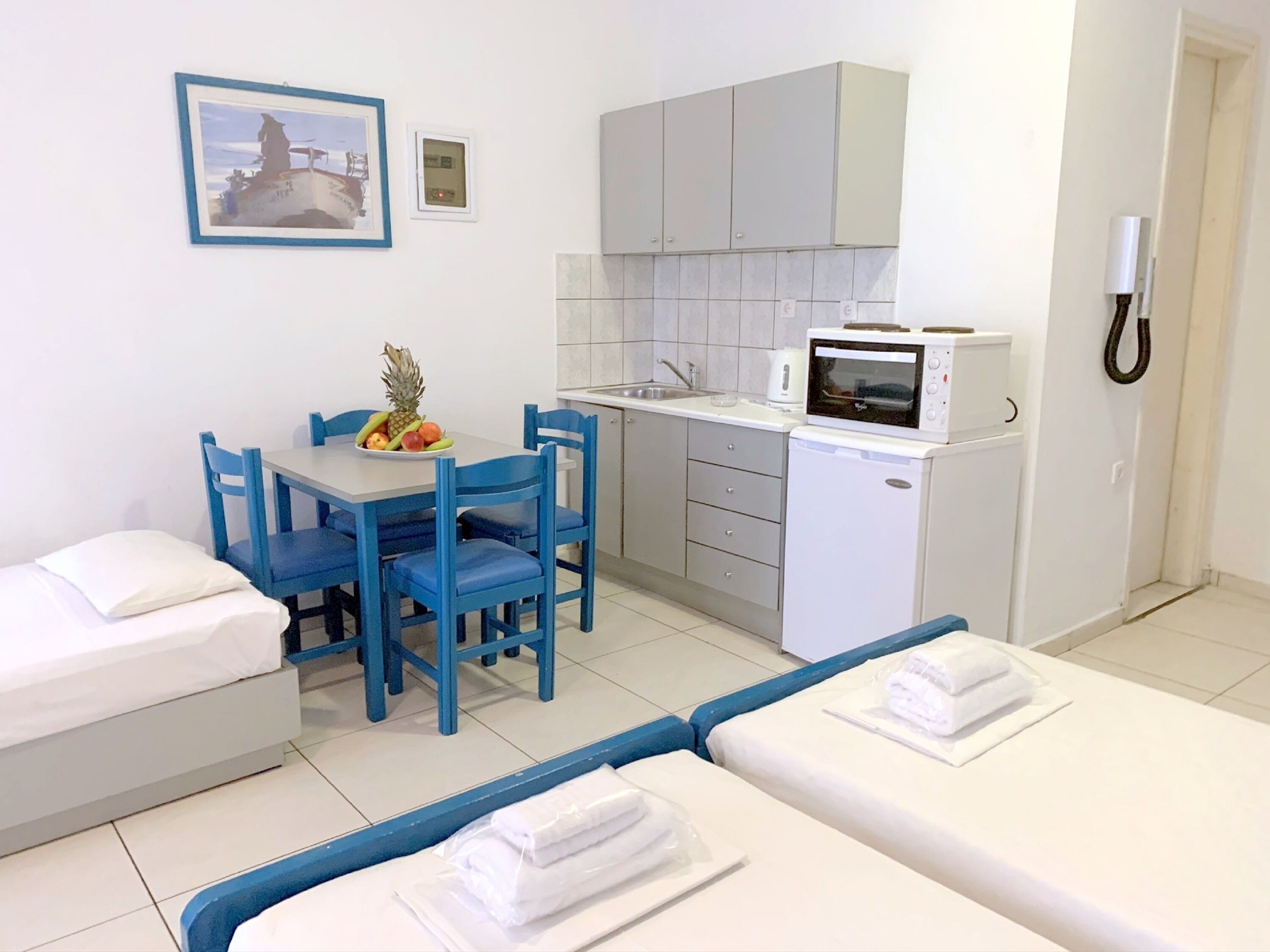 Een compacte hotelkamer met kitchenette, een zithoek met blauwe stoelen, een bed met witte lakens en een kleine badkamer.
