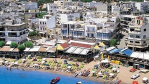Une ville côtière dotée d’une plage aménagée avec des transats et des parasols, des bateaux sur l’eau, et où se côtoient des bâtiments modernes et traditionnels.