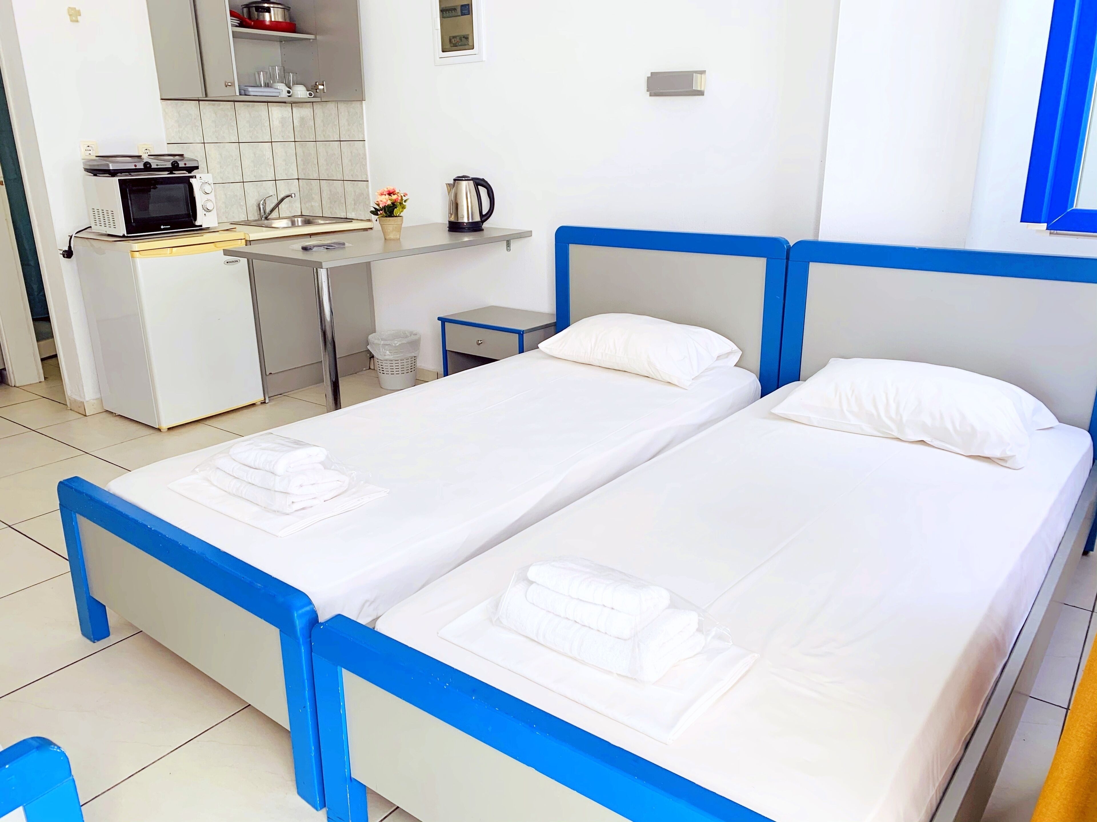 Habitación de hotel con dos camas, kitchenette y baño pequeño.