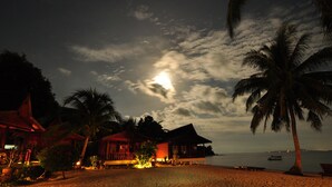 Un resort sulla spiaggia con bungalow sull'acqua, palme e un mare calmo di notte.