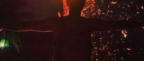 La silhouette d’une personne, les bras tendus, se tient face à un feu d’où jaillissent des étincelles.