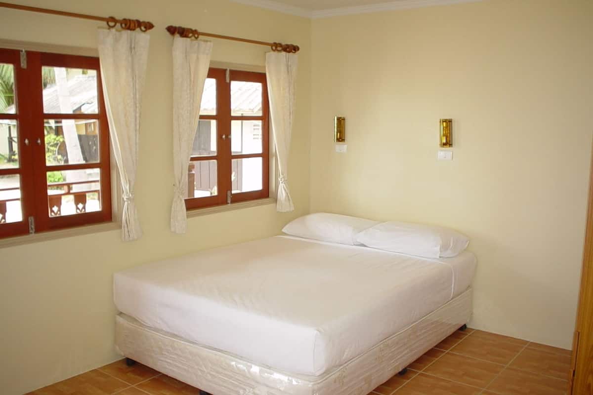 Un dormitorio con una cama individual, dos ventanas con cortinas y suelo de baldosas.