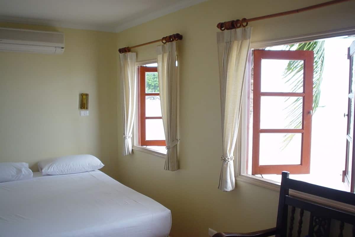Una habitación con una cama, dos ventanas con cortinas, una silla y un equipo de aire acondicionado.