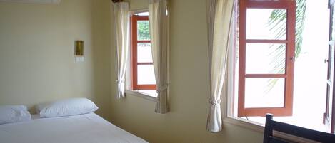 Una habitación con una cama, dos ventanas con cortinas, una silla y un equipo de aire acondicionado.