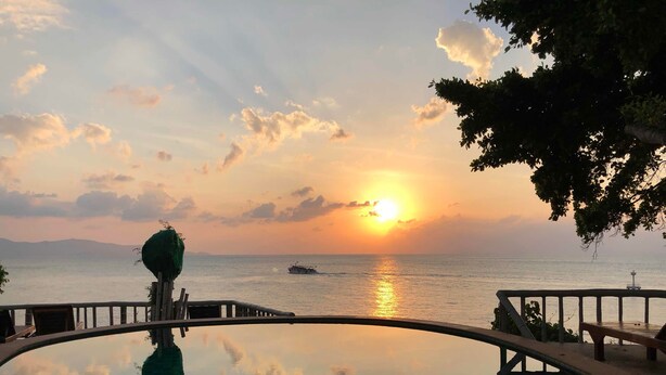A clear view of a sunset over the ocean, a boat on the water, and a pool reflecting the sky. - Suncliff Resort (Ko Pha-ngan)
