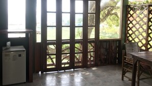 A room with a tiled floor, a refrigerator, a wooden table, and a window with a view of greenery. - Suncliff Resort (Ko Pha-ngan)