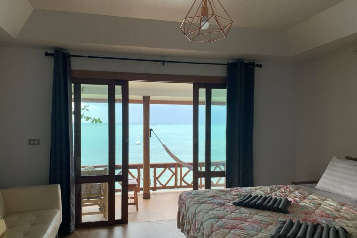 A bedroom with a bed, a sofa, and a view of the sea through a sliding door.