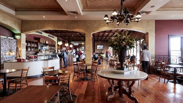 A restaurant with wooden tables and chairs, a bar area, and a large decorative vase. - The Terrace at The Settlement (Cranbourne)