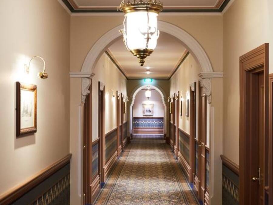 A long, narrow hallway with ornate wooden doors and a patterned carpet.