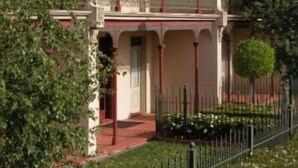 A two-story building with a balcony, a red entrance, and a small garden area. - The Terrace at The Settlement (Cranbourne)