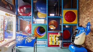 Kids can play and explore in this vibrant indoor play area featuring a spiral play tunnel, a claw machine, and a ride-on toy.