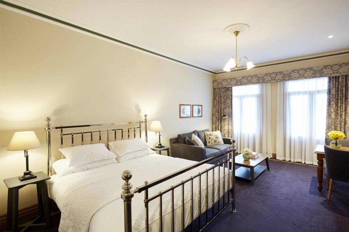A hotel room with a large bed, a sofa, a small table, and a desk.