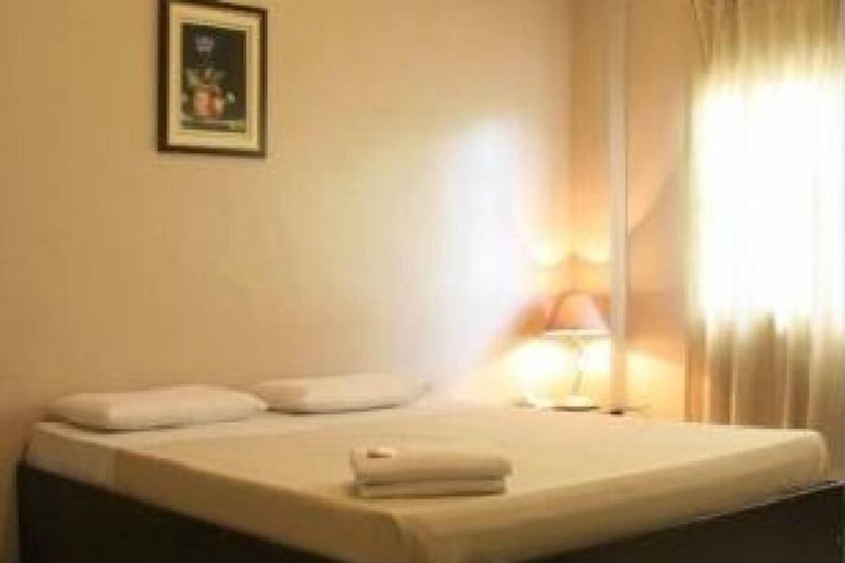 A neatly made bed with a white duvet and pillows, a bedside lamp, and a framed picture on the wall.