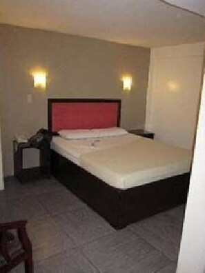 A hotel room with a single bed, a nightstand, a lamp, and a chair. - Toilena Room and Board (Manila)