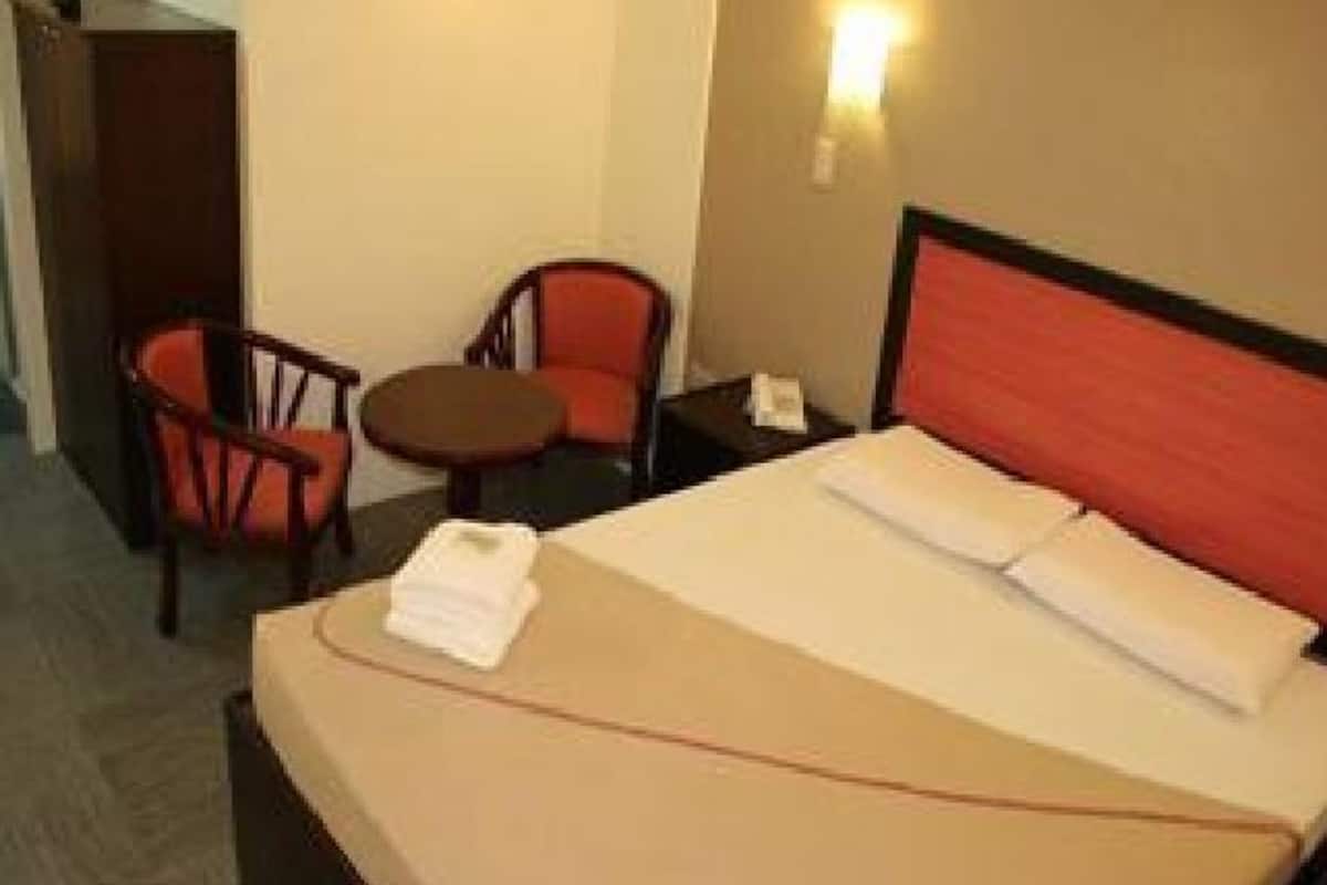 A hotel room with a bed, two chairs, a small table, and a nightstand.