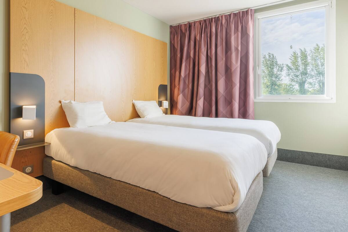 A hotel room with a bed, bedside tables, a desk, and a window with curtains.