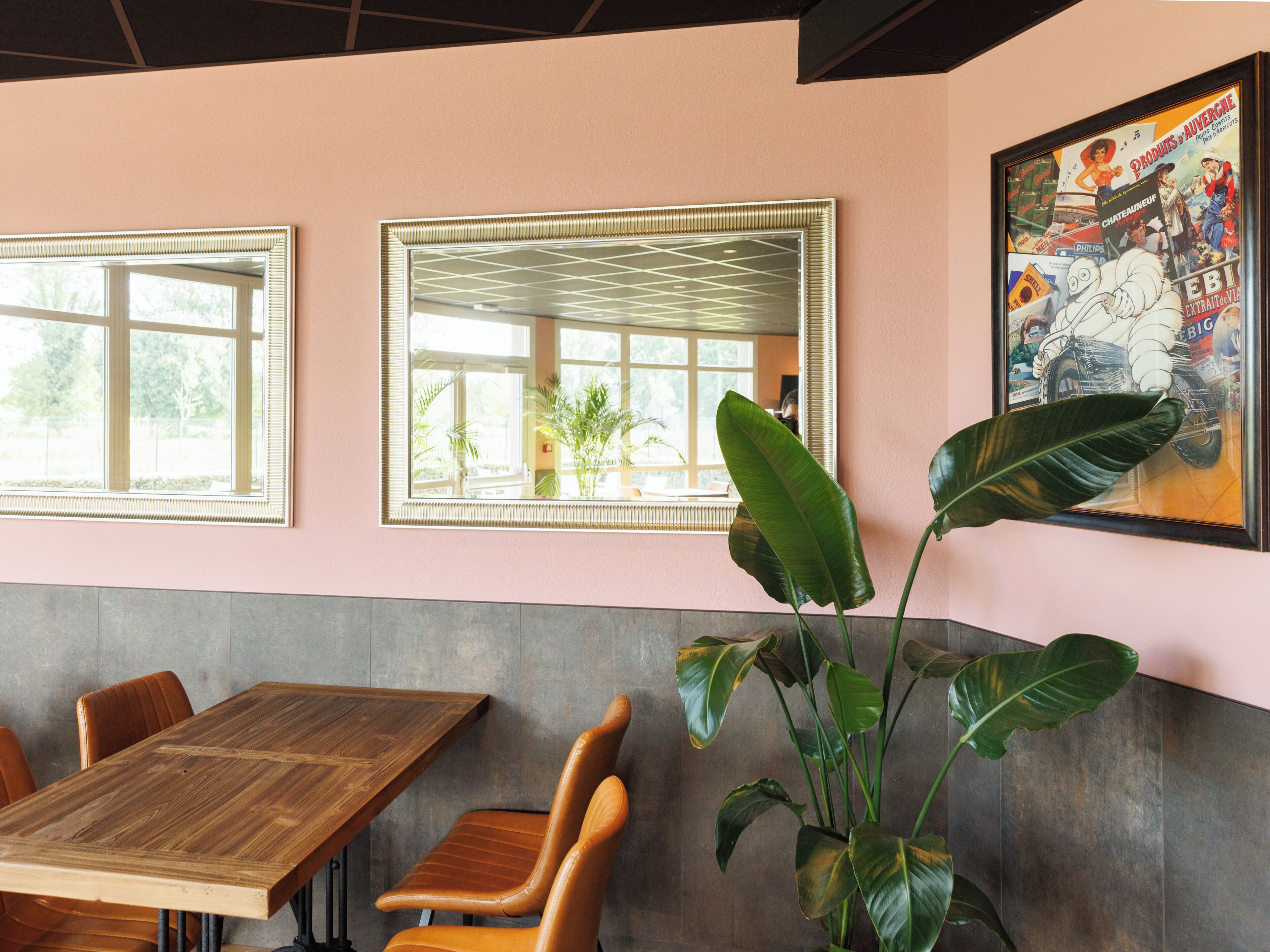 L'intérieur d'un restaurant avec une table en bois, des chaises, un grand miroir et un tableau encadré au mur.