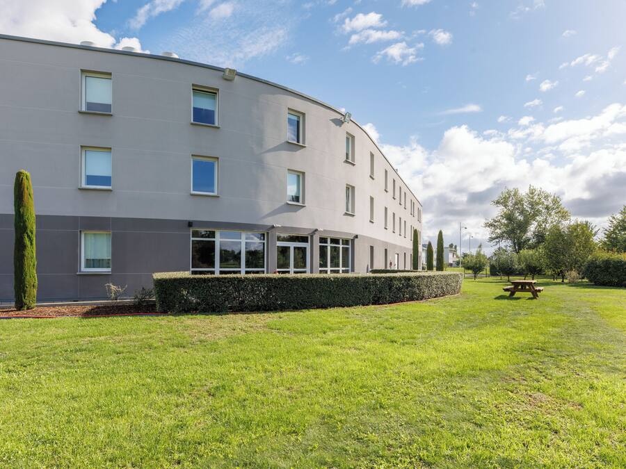Un edificio moderno con techo plano, varias ventanas y un césped bien cuidado con una mesa de picnic.