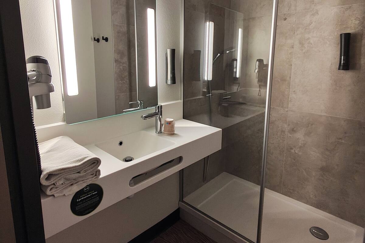 A modern bathroom with a large mirror, a white sink, a glass shower enclosure, and a towel rack.