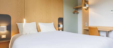 Une chambre d’hôtel moderne avec un grand lit, des lampes de chevet, une tête de lit en bois, un bureau avec une chaise et un miroir.