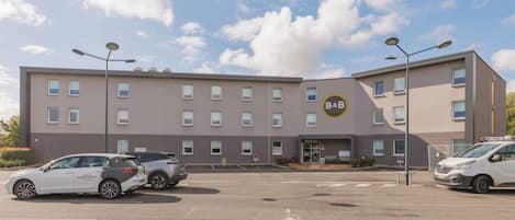 A B&B hotel with a modern design, featuring a central entrance and a parking lot with several cars.