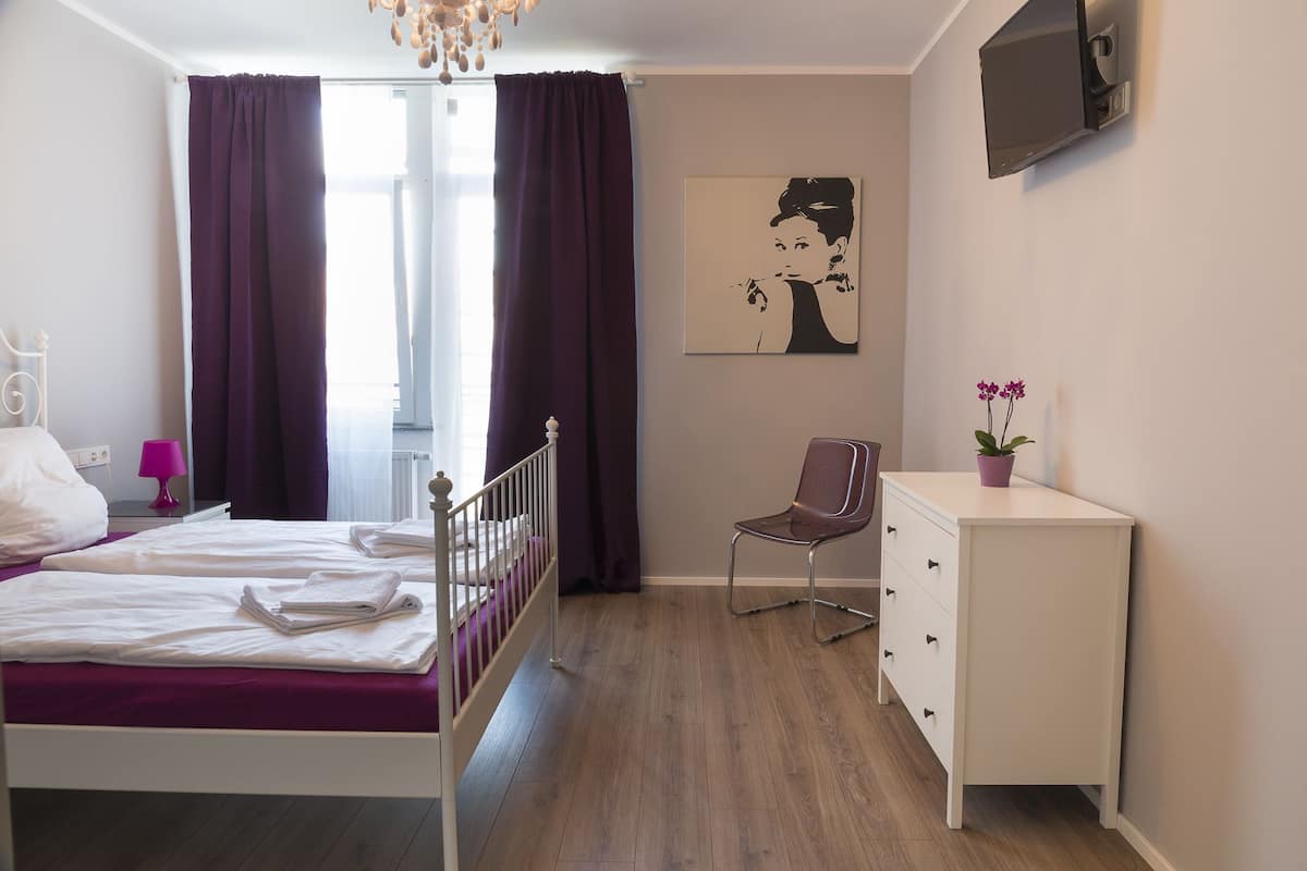 A bedroom with a bed, a chair, a dresser, a painting, and a TV.