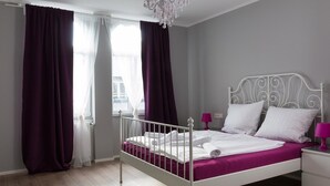 A bedroom with a white metal bed frame, a chandelier, a white nightstand, and purple curtains. - Hotel Forty Four (Frankfurt)
