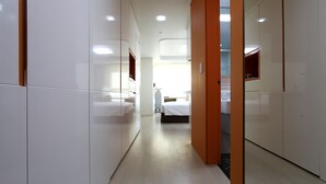 A hotel corridor with a bed, a chair, and a wardrobe.