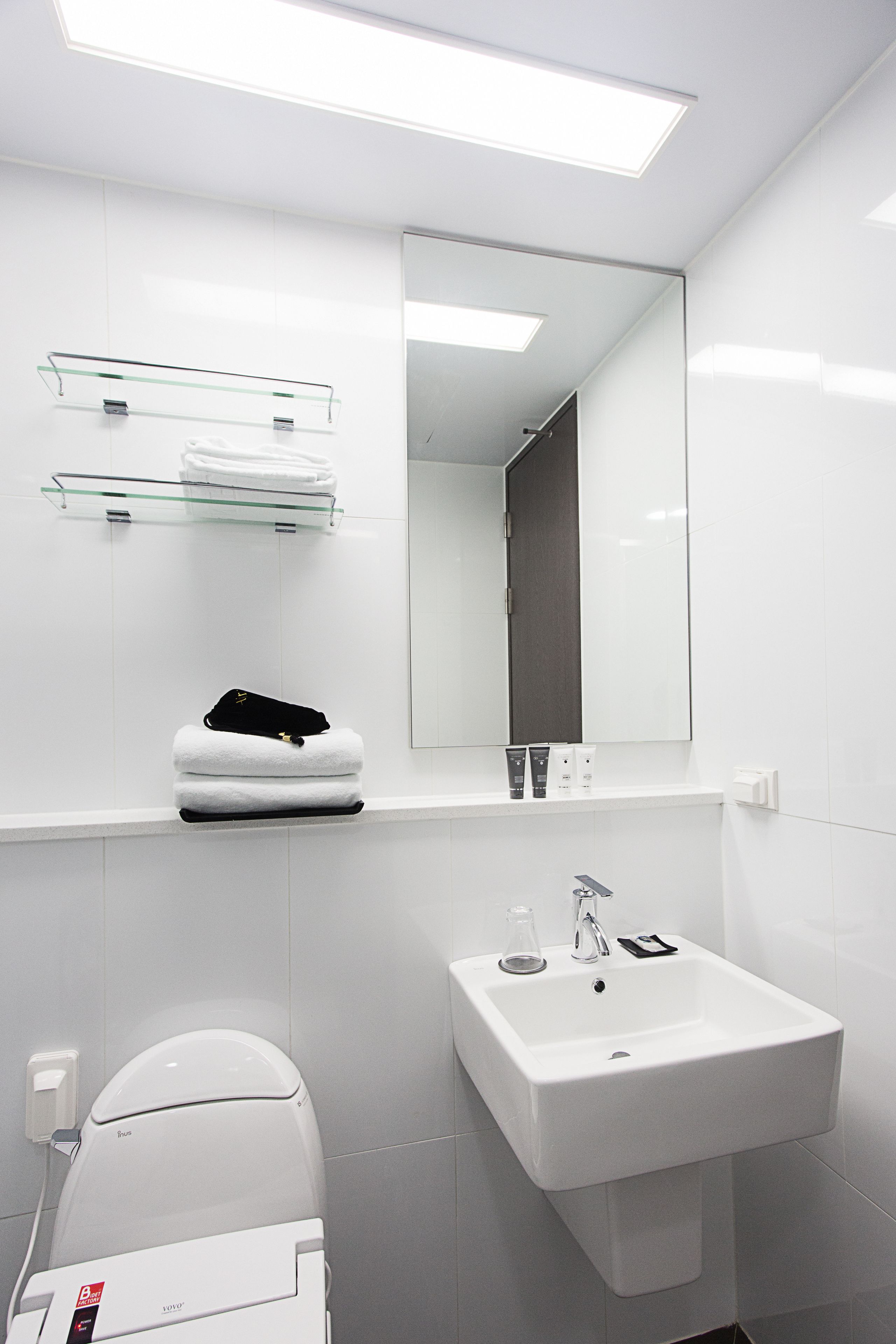 A modern bathroom with a white sink, a glass shelf with toiletries, and a toilet.
