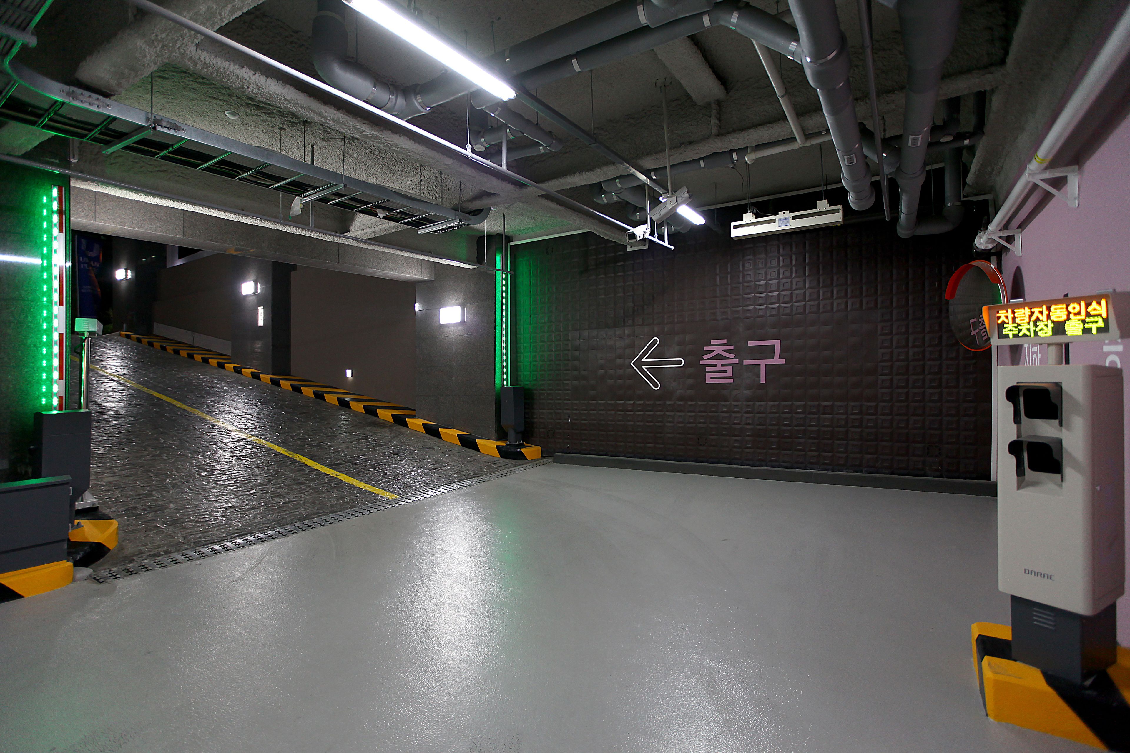 Un parking intérieur doté d’une signalisation claire indiquant les directions, d’une rampe menant à une zone de stationnement et d’un mur sur lequel est peinte une flèche directionnelle.