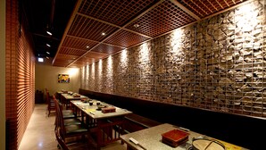 A restaurant with long tables and chairs, a stone wall, and a ceiling with a grid pattern.
