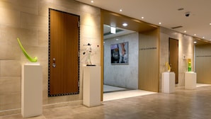 A modern hotel lobby with a wooden door, a green abstract sculpture, and a poster on the wall.