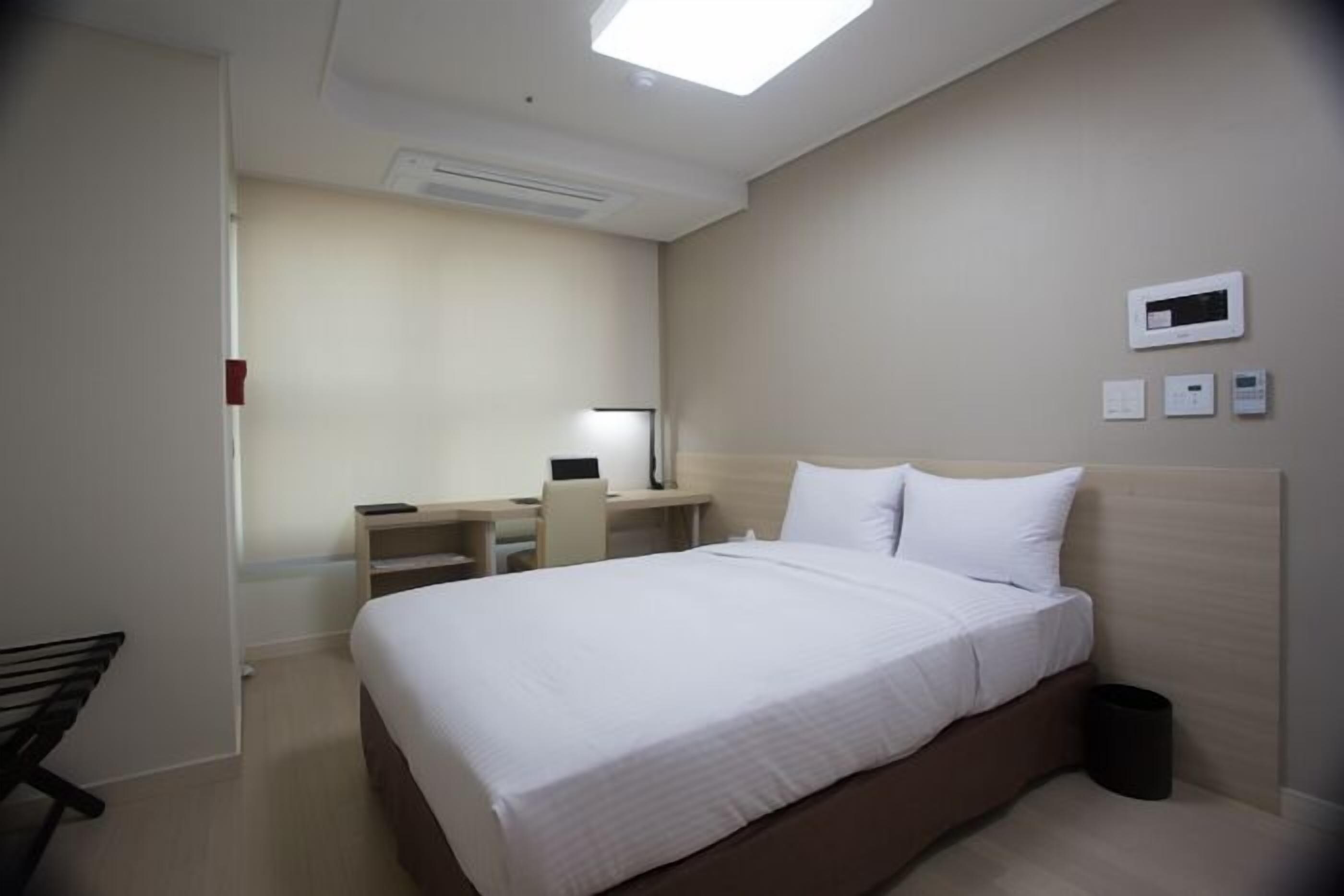 A hotel room with a bed, desk, chair, and a small table.