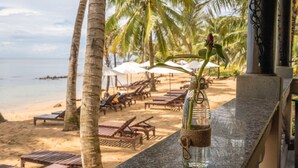A beachside view with palm trees, lounge chairs, and a bottle with a plant on a balcony. - Sea Sense Resort (Phu Quoc)