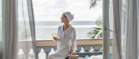 Una persona con un albornoz blanco sentada junto a una ventana con vista al océano.