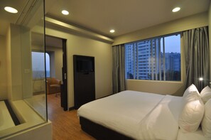 A hotel room with a large bed, a television, and a view of the cityscape through the window.
