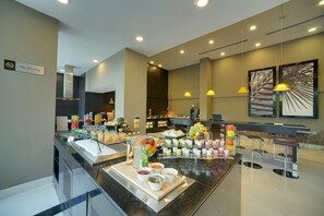 A buffet area with various food and drink options, a no-smoking sign, and modern lighting fixtures.