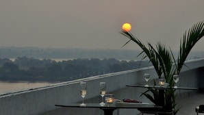 A table with two glasses and a candle, overlooking a river and sunset.