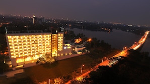 A modern hotel with a large number of illuminated rooms, situated near a river with a bridge in the background.