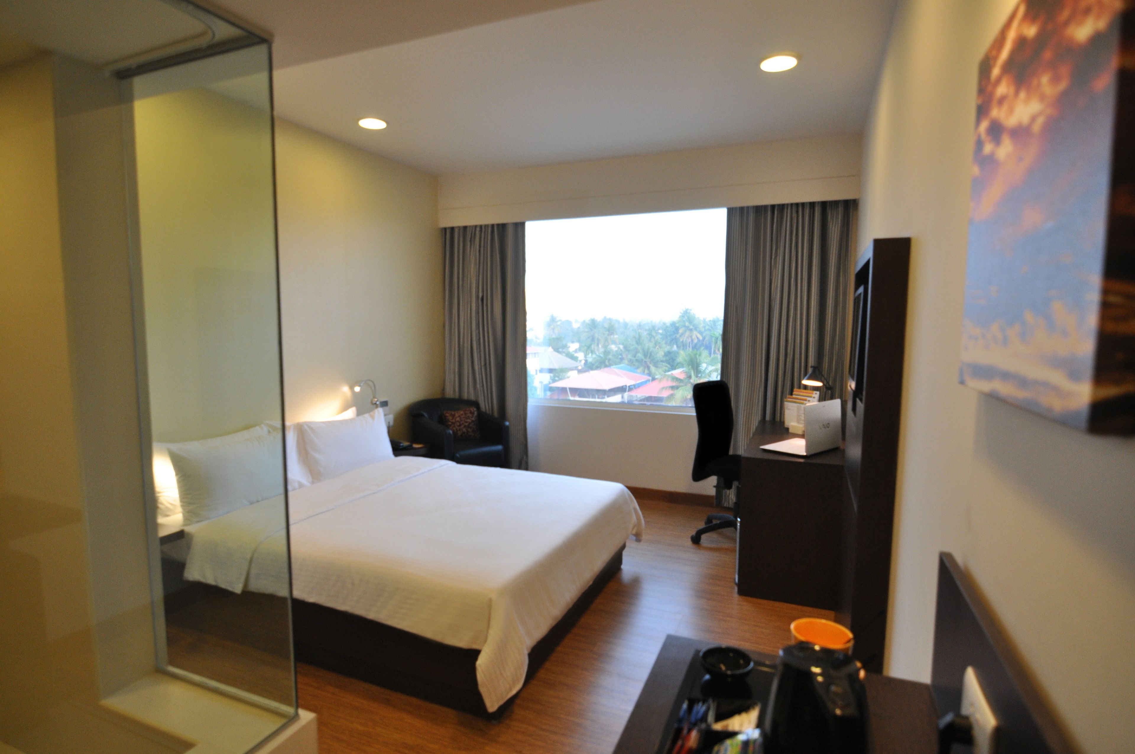 Habitación de hotel con una cama grande, un escritorio, una silla, un espejo y una ventana con cortinas.