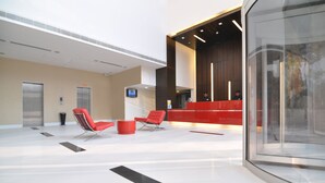 A modern lobby with two elevators, a reception desk, and red chairs.
