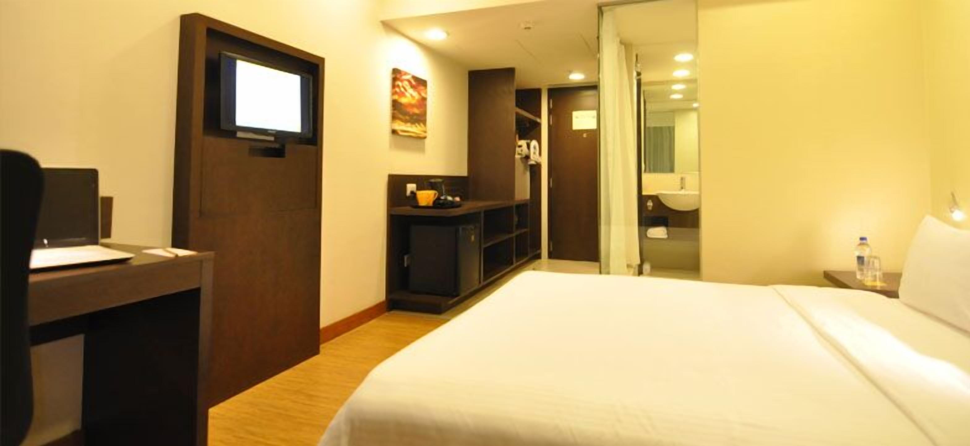 A hotel room with a bed, a desk, a TV, a wardrobe, and a bathroom.