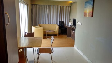 A hotel room with a dining area, a sofa, a TV, and a painting of a sunset.