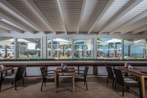 Ein Restaurant mit Außenbereich, großen Fenstern und Blick auf einen Pool und Palmen.