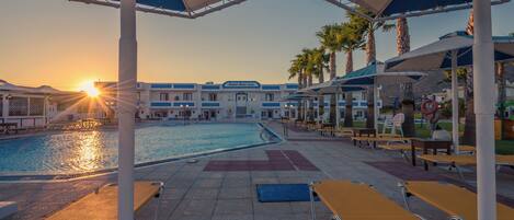 A poolside area with umbrellas, lounge chairs, and a pool.